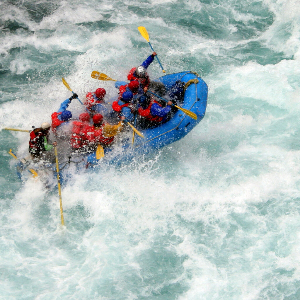 Advanced rafters in lifejackets and helmets paddling up towards the breaking waves in very choppy waters.